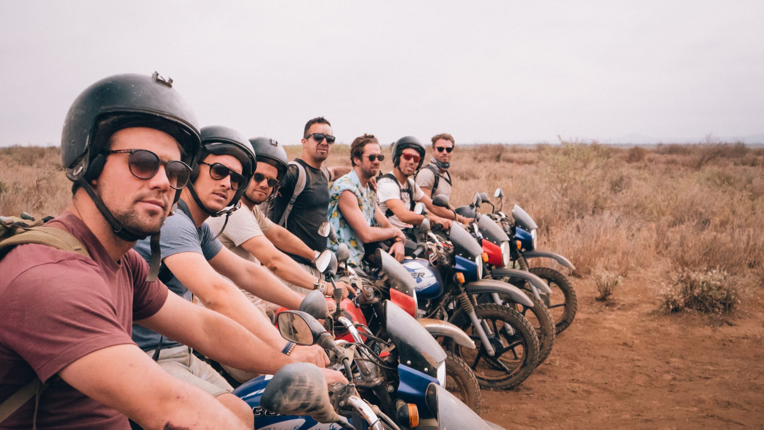 groep mannen met helmen poseren op motoren in droog savannelandschap in kenia
