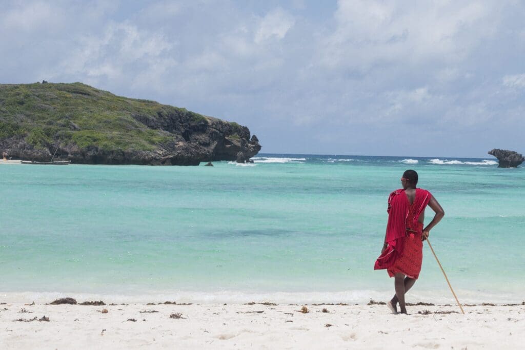masai in rode shuka kijkt uit over turquoise oceaan bij rotsachtige kust in Kenia