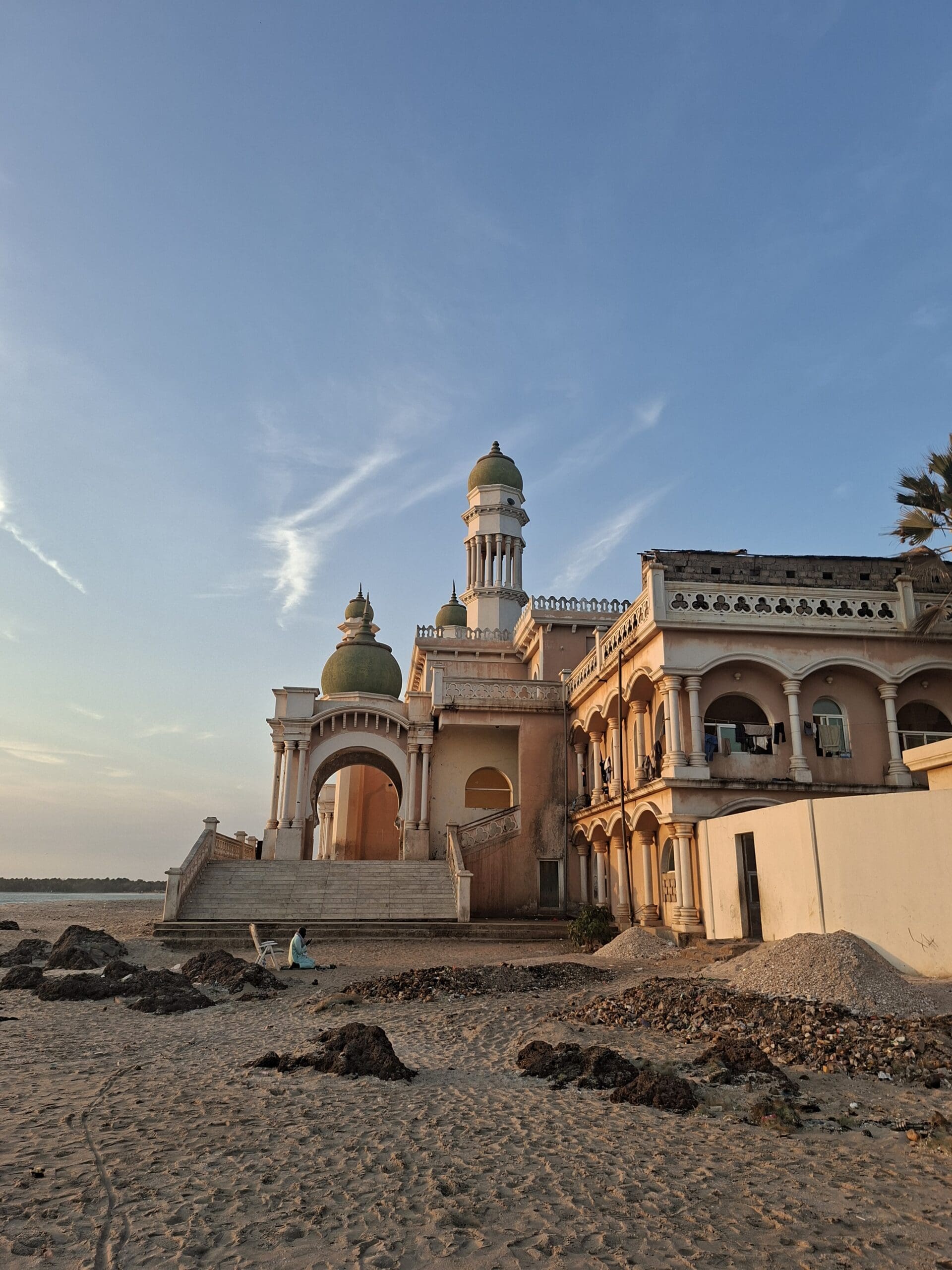 Een man met kort bruin haar en een baard glimlacht, draagt een lichtgeel overhemd over een wit t-shirt en staat tegen een effen witte achtergrond.