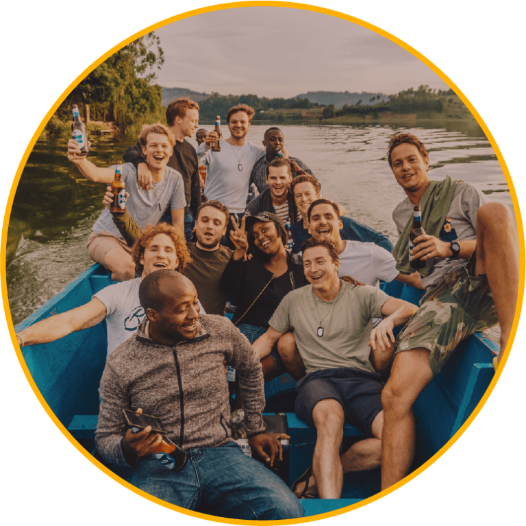 Een groep vrienden glimlacht en houdt drankjes vast terwijl ze samen op een blauwe boot zitten in een schilderachtige omgeving van een meer bij zonsondergang, omringd door groen en kalm water.